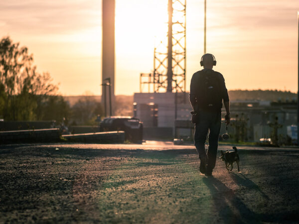 A person walking their dog on a lead along a suburban street in the evening light