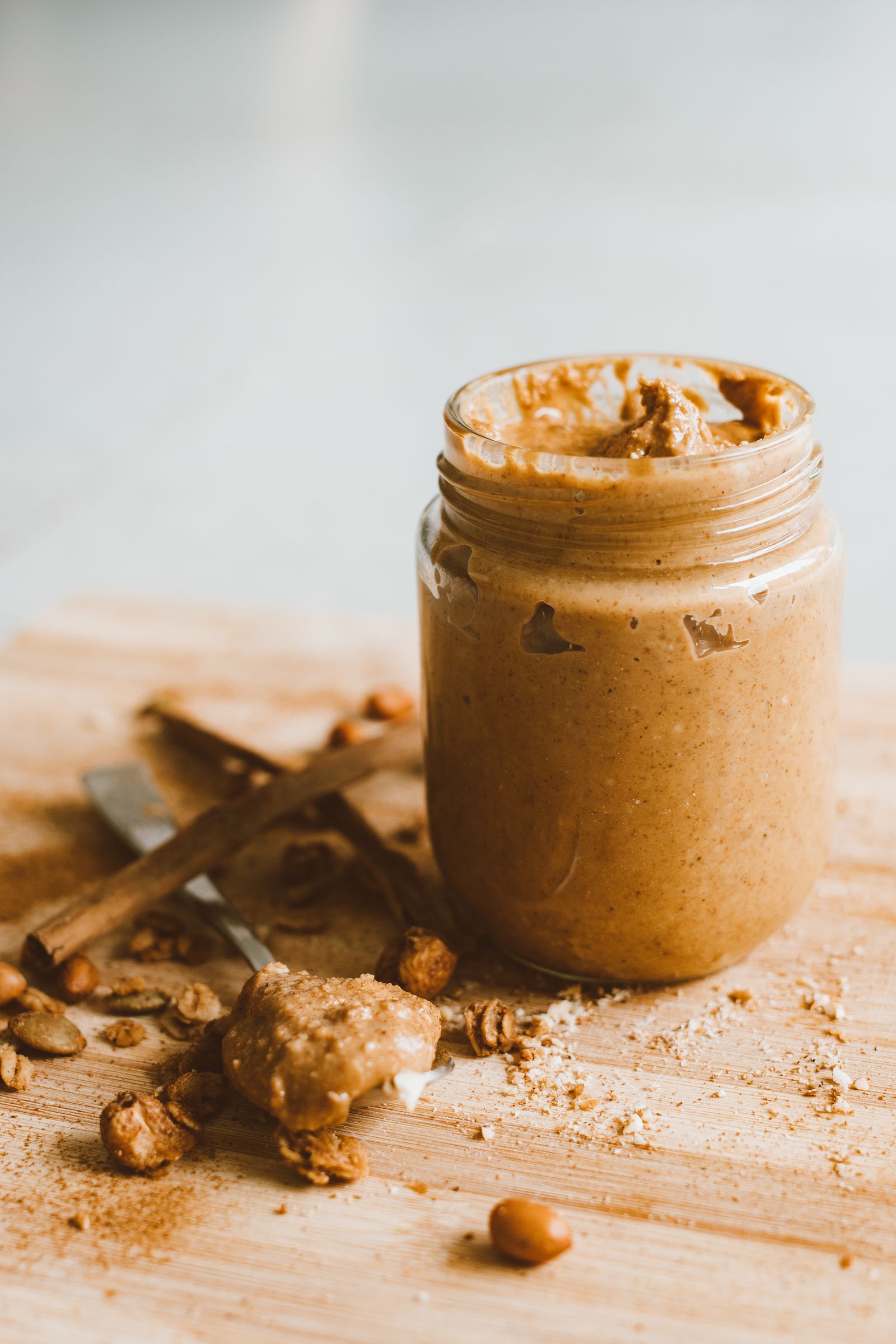 Open glass jar of plain peanut butter with peanuts on a wooden bench