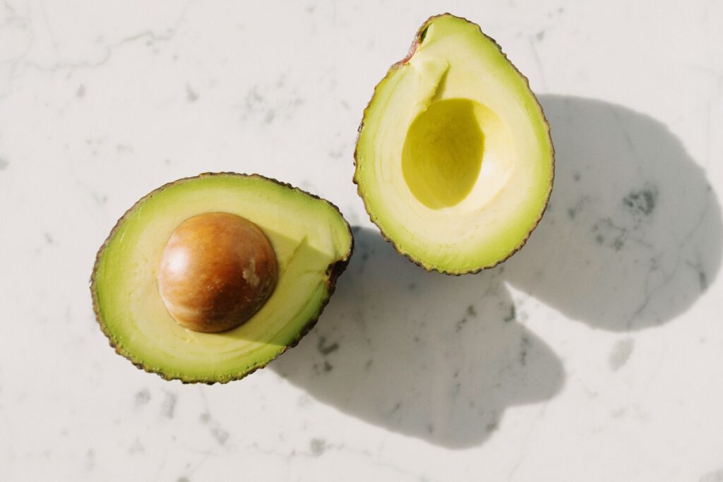 Two avocado halves on a white marble surface, one holding the large brown pit