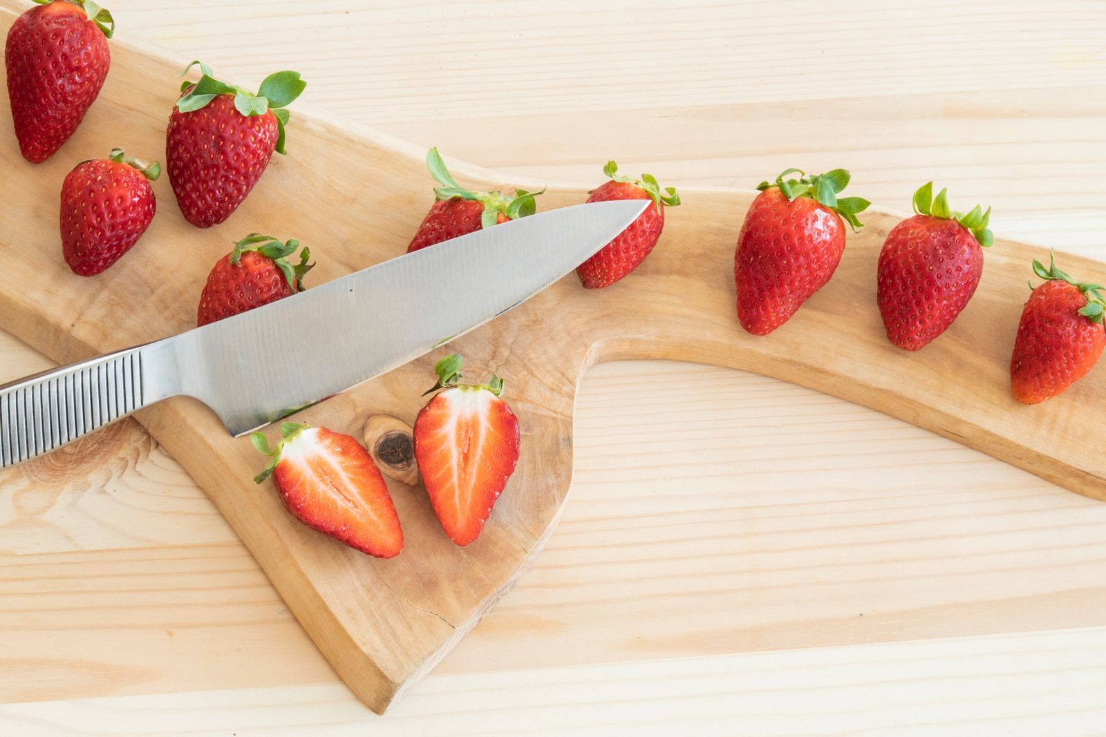 Fresh strawberries on a wooden chopping board with one cut in half next to a knife