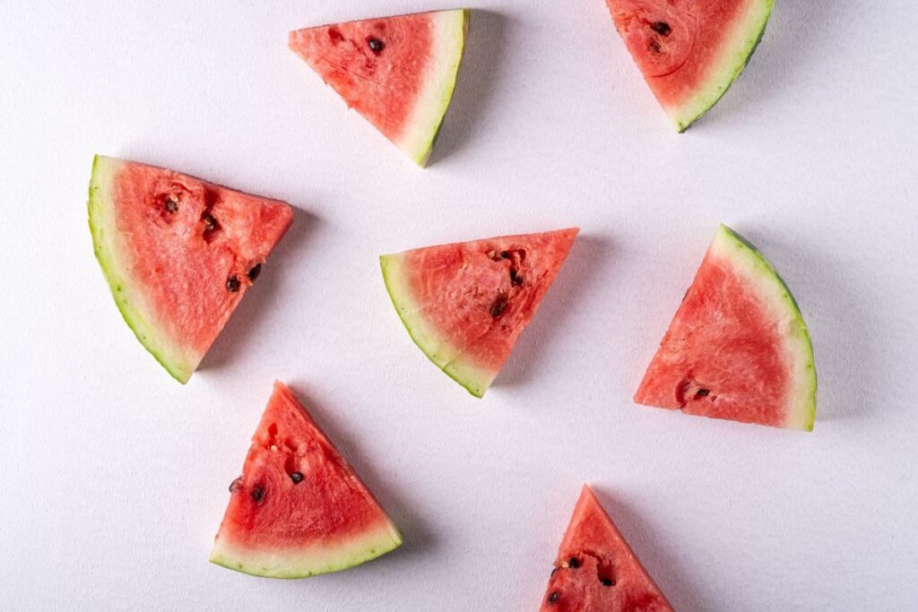 Watermelon wedges with green rind and black seeds laid out on a white background