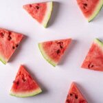 Watermelon wedges with green rind and black seeds laid out on a white background