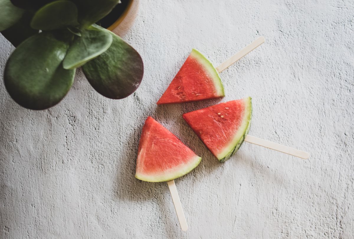 Three watermelon wedges on wooden ice block sticks next to a potted plant